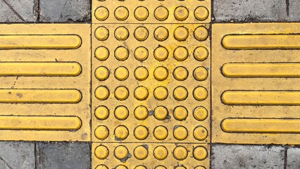 Yellow tactile paving with dot and line patterns for visually impaired pedestrian safety on a...