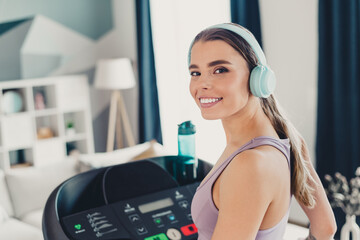 Young woman in activewear enjoying workout on treadmill at home while listening to music with headphones