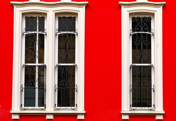Fototapeta premium Vibrant red facade, crisp white windows framed by intricate wrought iron grilles, texture, surface