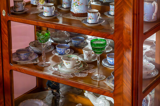 Porcelain cups and stemware displayed inside glass cabinet in classic wooden dining room interior with collection