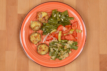 An orange plate holds a meal consisting of stuffed mushrooms, a cooked green bean and garlic salad, a fresh green bean and tomato salad, and green beans with breadcrumbs and cream
