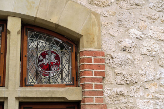 Kraków, Poland. A section of a historic stone building featuring three arched windows with decorative stained glass depicting a knight on horseback. - Powered by Adobe