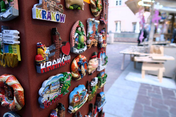 Tourist in christmas market checking a display of colorful ceramic fridge magnets featuring hand-painted depictions of Kraków, Poland, arranged on a metallic surface 