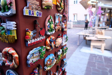 Tourist in christmas market checking a display of colorful ceramic fridge magnets featuring hand-painted depictions of Kraków, Poland, arranged on a metallic surface 