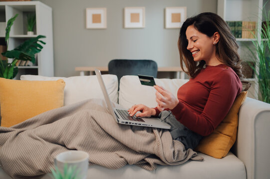 Smiling woman using laptop and credit card on sofa at home