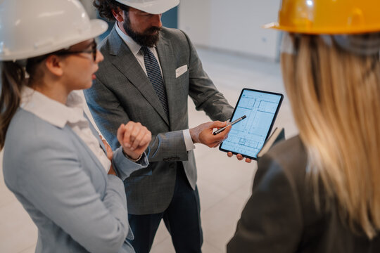 Architects and engineers discussing blueprint on tablet at construction site