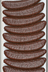 Chocolate-covered banana-shaped candies are neatly arranged in a cardboard box, ready for sale or...