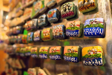Tourist in christmas market checking a display of colorful ceramic fridge magnets featuring hand-painted depictions of Kraków, Poland, arranged on a metallic surface 