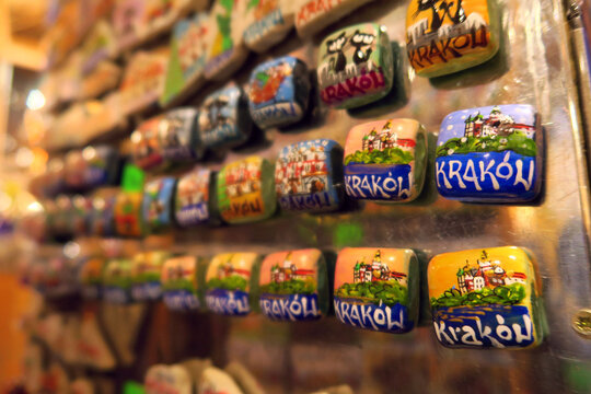 Tourist in christmas market checking a display of colorful ceramic fridge magnets featuring hand-painted depictions of Krak&oacute;w, Poland, arranged on a metallic surface 