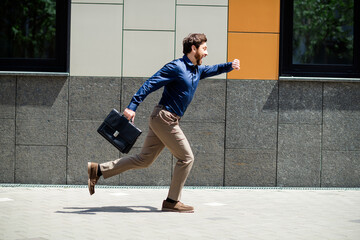 Businessman running along an urban street carrying a briefcase during a sunny day, symbolizing...