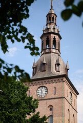 Historic Brick Clock Tower of Oslo Cathedral Framed by Green Foliage on a Clear Summer Day in Norway