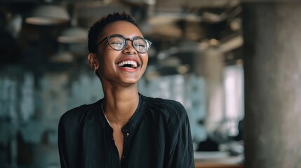 Fototapeta premium young african businesswoman wearing glasses and laughing while standing alone in a modern office no logos no brands ar 169