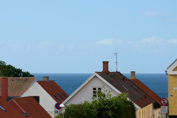Rooftops of traditional Danish houses with red and white facades overlooking the Baltic Sea horizon under blue sky in Bornholm Denmark
