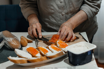 Close-up female hands make sandwiches with bread and butter or soft cheese and salmon fillets.