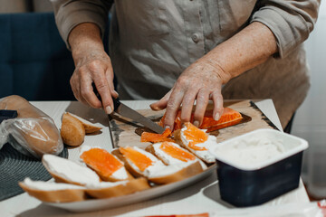 Close-up female hands make sandwiches with bread and butter or soft cheese and salmon fillets.