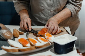 Close-up female hands make sandwiches with bread and butter or soft cheese and salmon fillets.