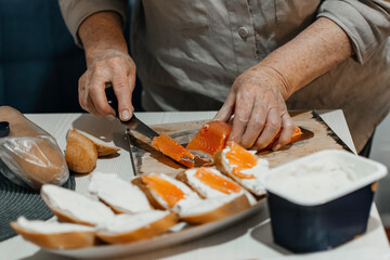 Close-up female hands make sandwiches with bread and butter or soft cheese and salmon fillets.