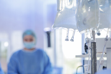 IV fluid bags on stand in operating room with surgeon in background