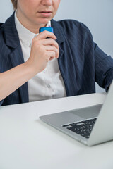 Business woman smoking an electronic cigarette while working on a laptop. Tobacco heating system.