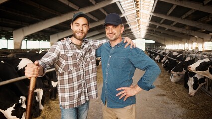 Two happy Caucasian male farmers working at farm standing in cowshed and smiling to camera. Joyful...