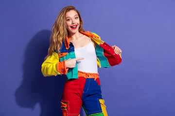 Young cheerful woman in vibrant patchwork outfit confidently posing against a purple background