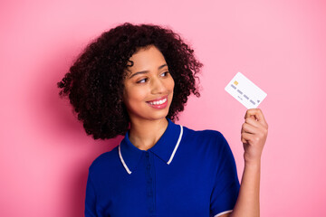 Smiling young woman in blue t-shirt holding a credit card posed against a vibrant pink background