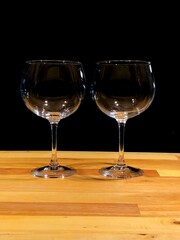 Two empty wine glasses on a wooden table with a dark background