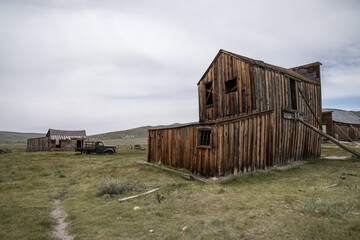 Weathered wooden buildings and an abandoned vintage truck in Bodie State Historic Park, California. This preserved ghost town, once a thriving gold-mining settlement, now a historic reminder.