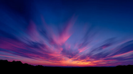 Fototapeta premium Radiant twilight sky ablaze with vibrant pink purple and orange clouds streaking across a deep blue expanse above a dark silhouetted landscape