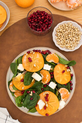 Winter salad. Fresh persimmon and pomegranate spinach salad with feta and pine nuts. Copy space