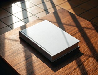 Fototapeta premium Blank white book resting on a wooden table with sunlight and shadows