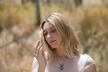 Portrait of a young, beautiful blonde woman with a serene gaze holding a dry, soft ear of corn in...