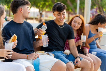 Group of generation z friends enjoying drinks and snacks together outdoors