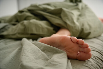 Man's foot peeking out from under cozy green sheets