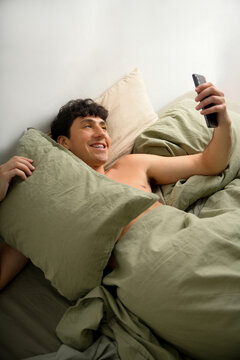 Young man relaxing in bed with his phone