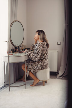 Mature woman applying makeup in front of a mirror