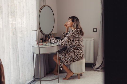 Mature woman applying makeup in front of a mirror