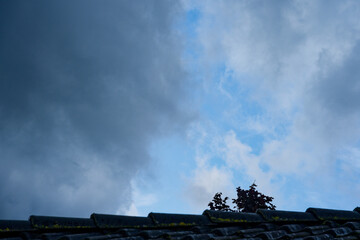 Old tiled roof with moss under blue sky and approaching gray clouds