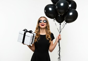 A beautiful woman holding a gift and black balloons, ready to celebrate and smile.