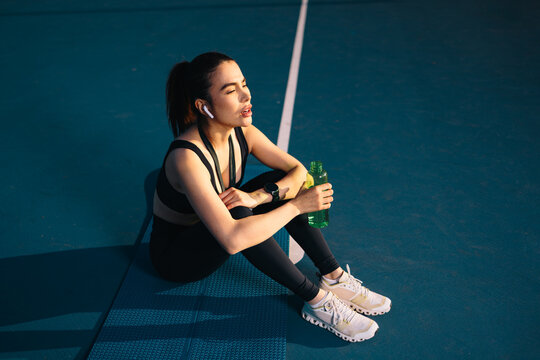 Young woman resting after training session on a paddle holding an energy drink bottle outdoors