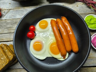 Delicious fried eggs with sausages served on a frying pan on a wooden table
