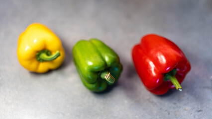 Vibrant trio of fresh whole bell peppers (yellow, green, red) on a rustic countertop. Perfect for healthy food ads, recipe books, and market visuals.