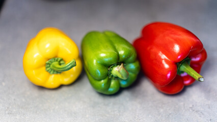 Vibrant trio of fresh whole bell peppers (yellow, green, red) on a rustic countertop. Perfect for healthy food ads, recipe books, and market visuals.