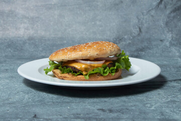Classic Cheeseburger on a White Plate with Beef patty, Lettuce, Onion, and a Sesame Seed Bun side view of American cuisine