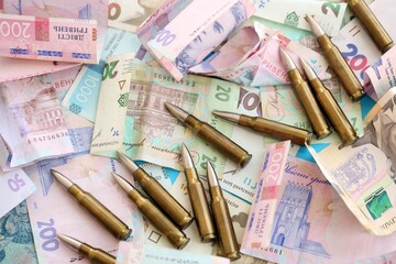 Many rifle bullets lies on lots of ukrainian money bills close up