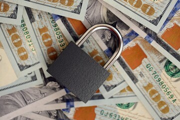 Small black padlock lies on big amount of new hundred US dollar bills