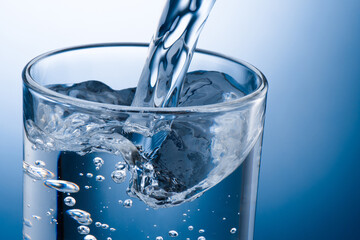 Pouring water into glass on blue background