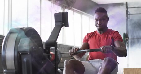 Gym athlete adjusting grip and feet initiating rowing machine strokes for stamina amid mist swirl - Powered by Adobe