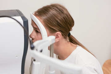 Child placing chin on a slit lamp or autorefractor during an eye examination at an ophthalmology...