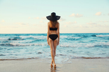 Summer vacation, rear view of beautiful young woman standing in swimsuit, slim girl on beach on sea